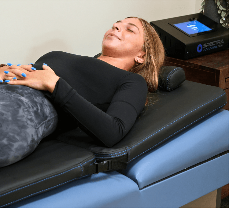 Guest relaxing on the PEMF therapy mat beside the control unit